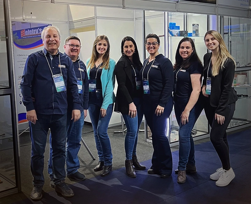 24 anos de mercado Parte da equipe da Eletru's em frente ao stand em feira.